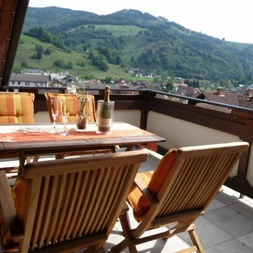 Balkon mit Holztisch und vier St&uuml;hlen im Hintergrund der Blick auf die gr&uuml;nen W&auml;lder und Wiesen - 