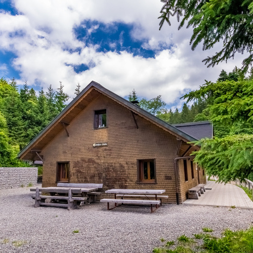 Au&szlig;enansicht der H&uuml;tte mit Vorplatz mit zwei gro&szlig;en Holztischen und B&auml;nken  - 
